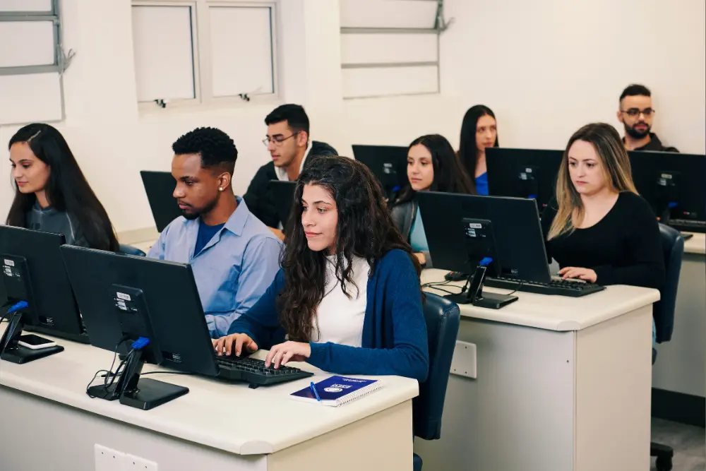 Alunos da Faculdade ESEG em uma aula de informática, concentrados em atividades nos computadores, refletindo o foco no aprendizado prático da Faculdade do Grupo Etapa.