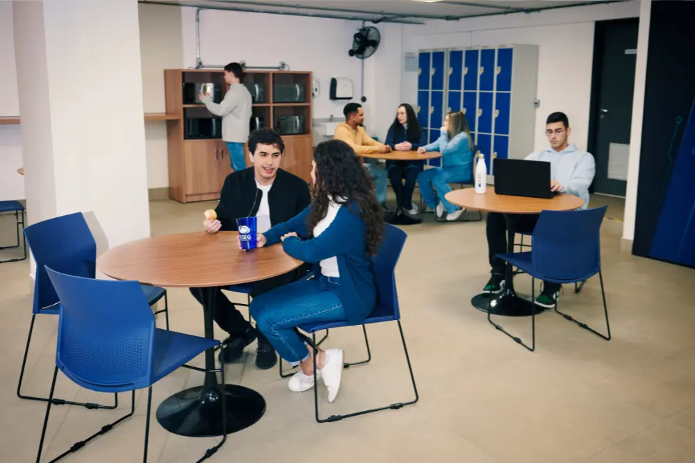 Estudantes da Faculdade ESEG no espaço de convivência, conversando e utilizando laptops, refletindo o ambiente acolhedor e colaborativo da Faculdade do Grupo Etapa